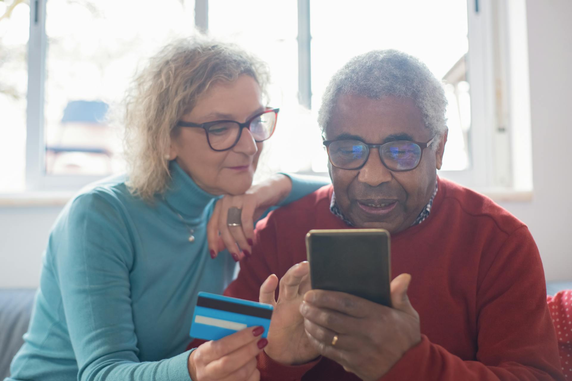 Senior couple using smartphone for online shopping with credit card indoors.