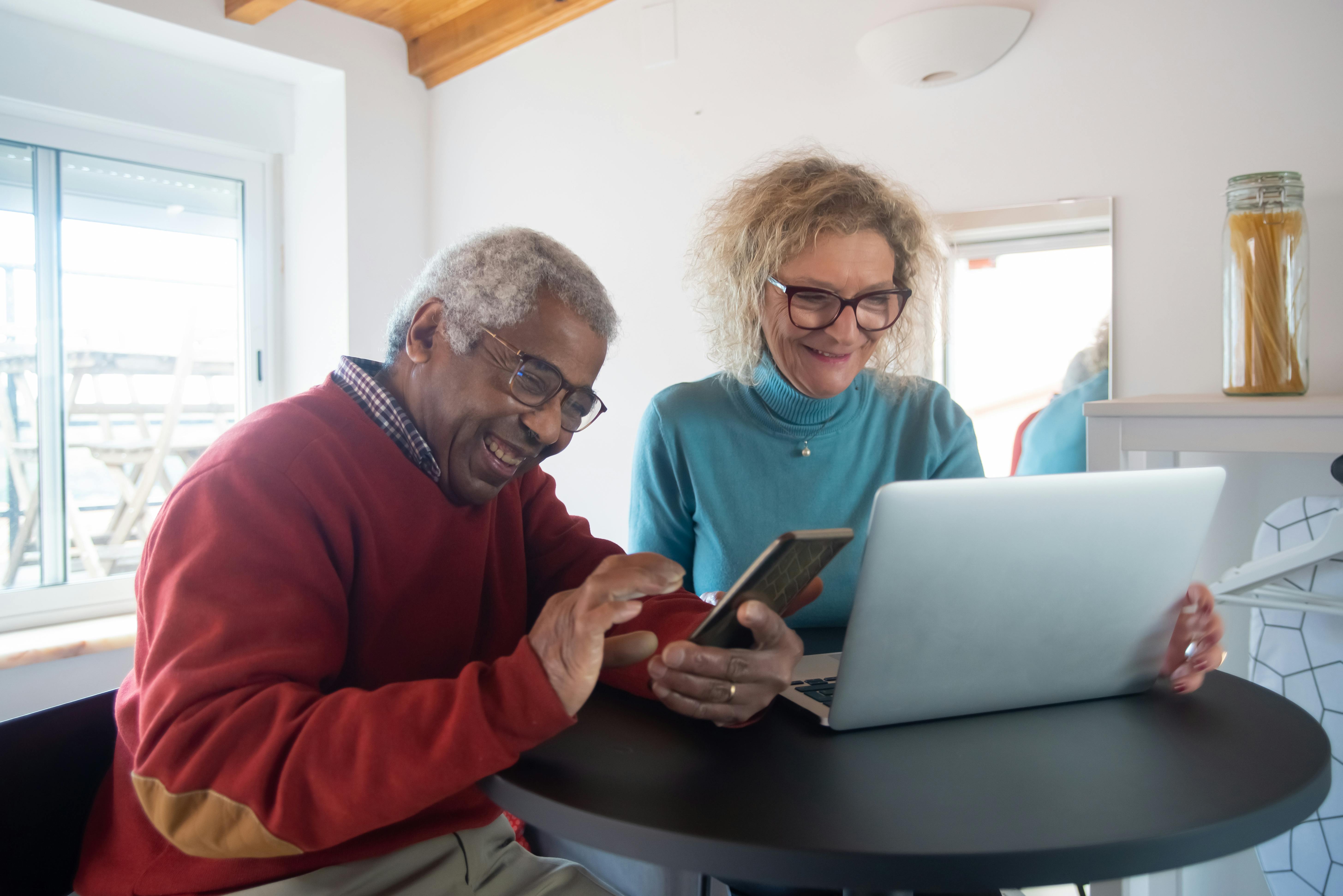 man and woman laughing while using gadgets