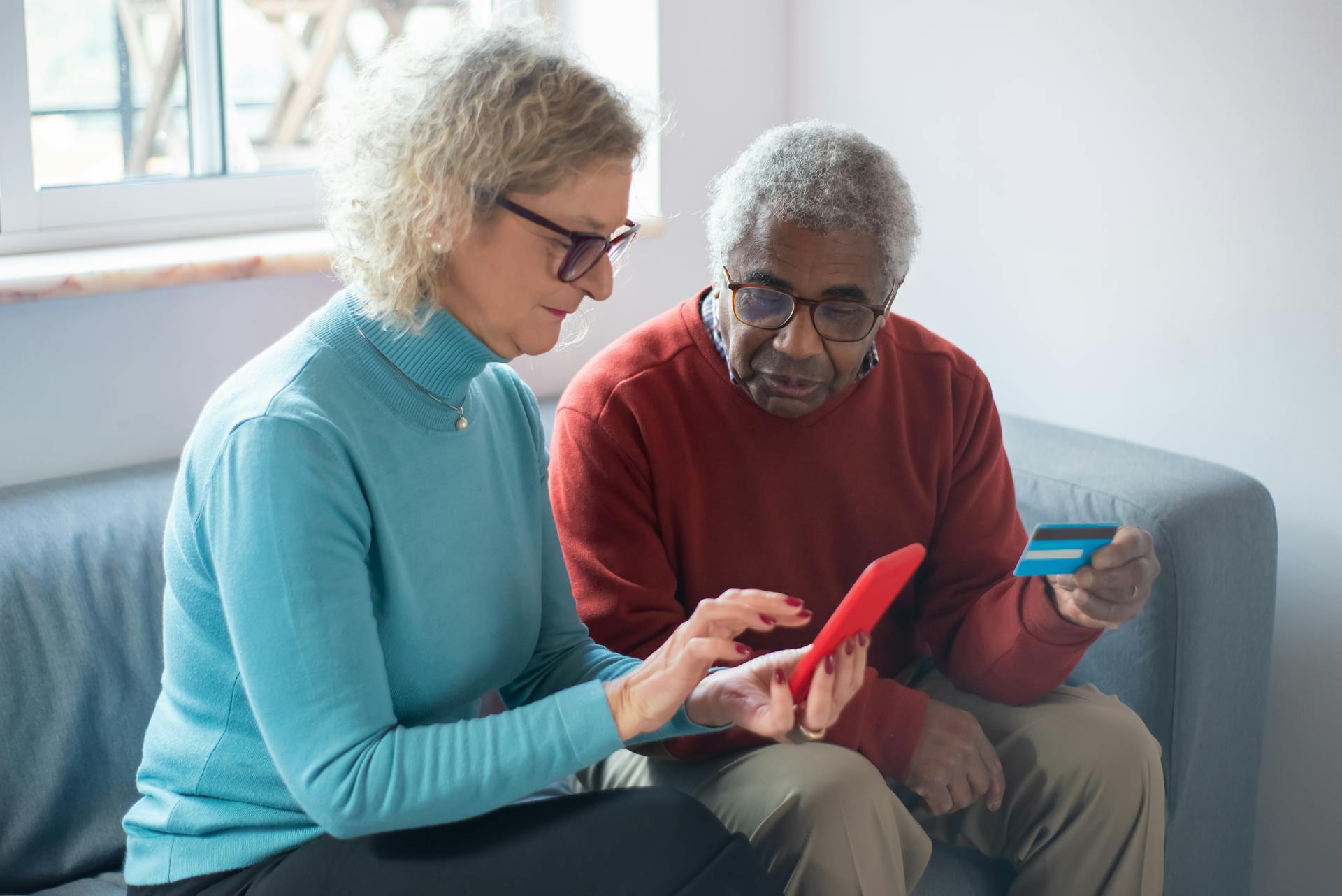 Elderly couple using a smartphone for online shopping, holding a credit card.