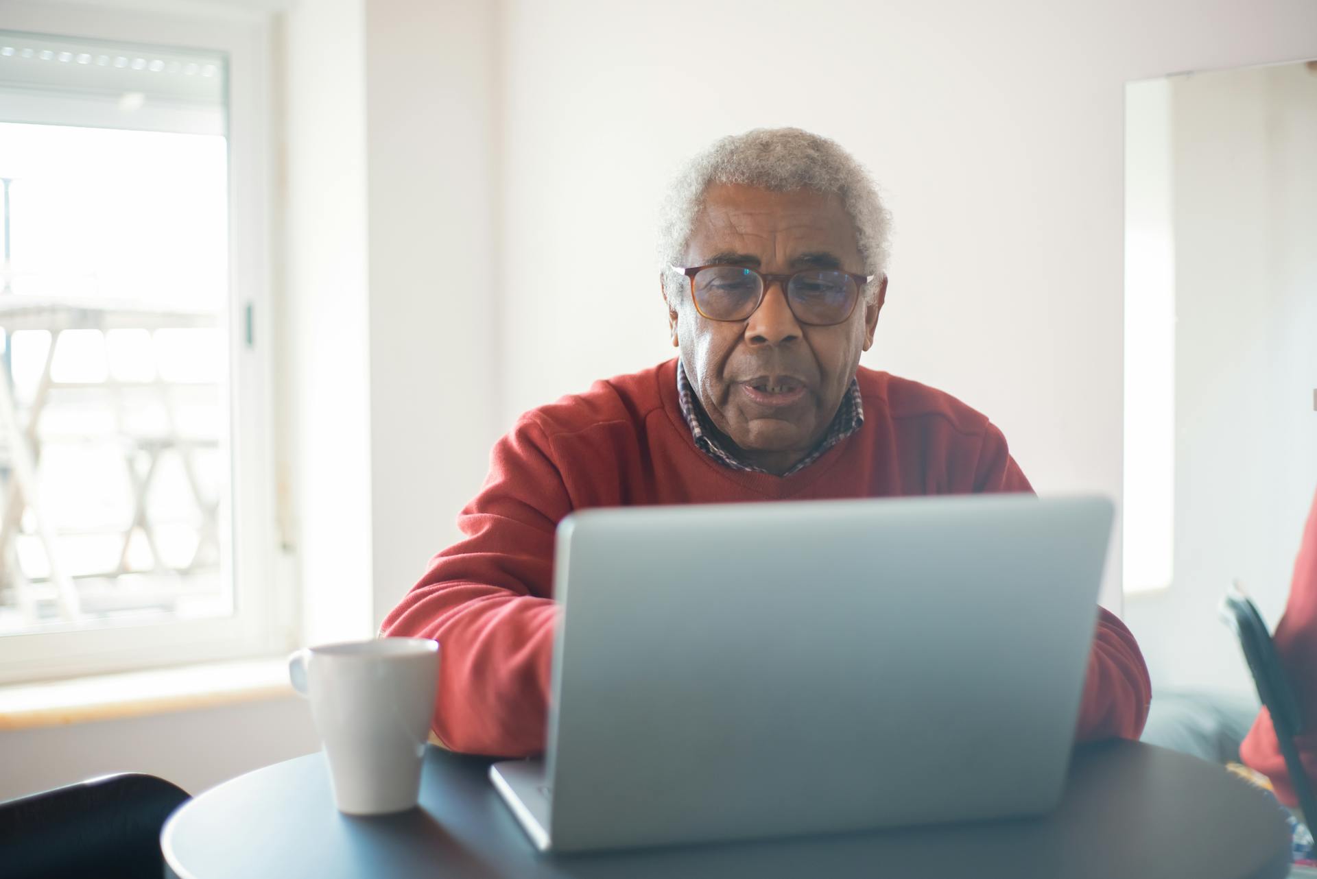 A senior man with eyeglasses using a laptop indoors for online shopping. Cozy and tech-savvy retirement lifestyle.