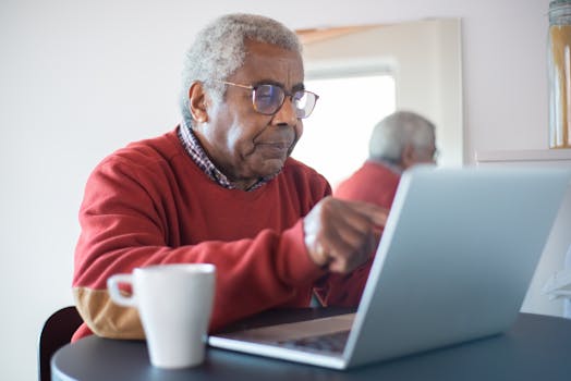 Senior man with eyeglasses intently using a laptop at home, reflecting concentration.