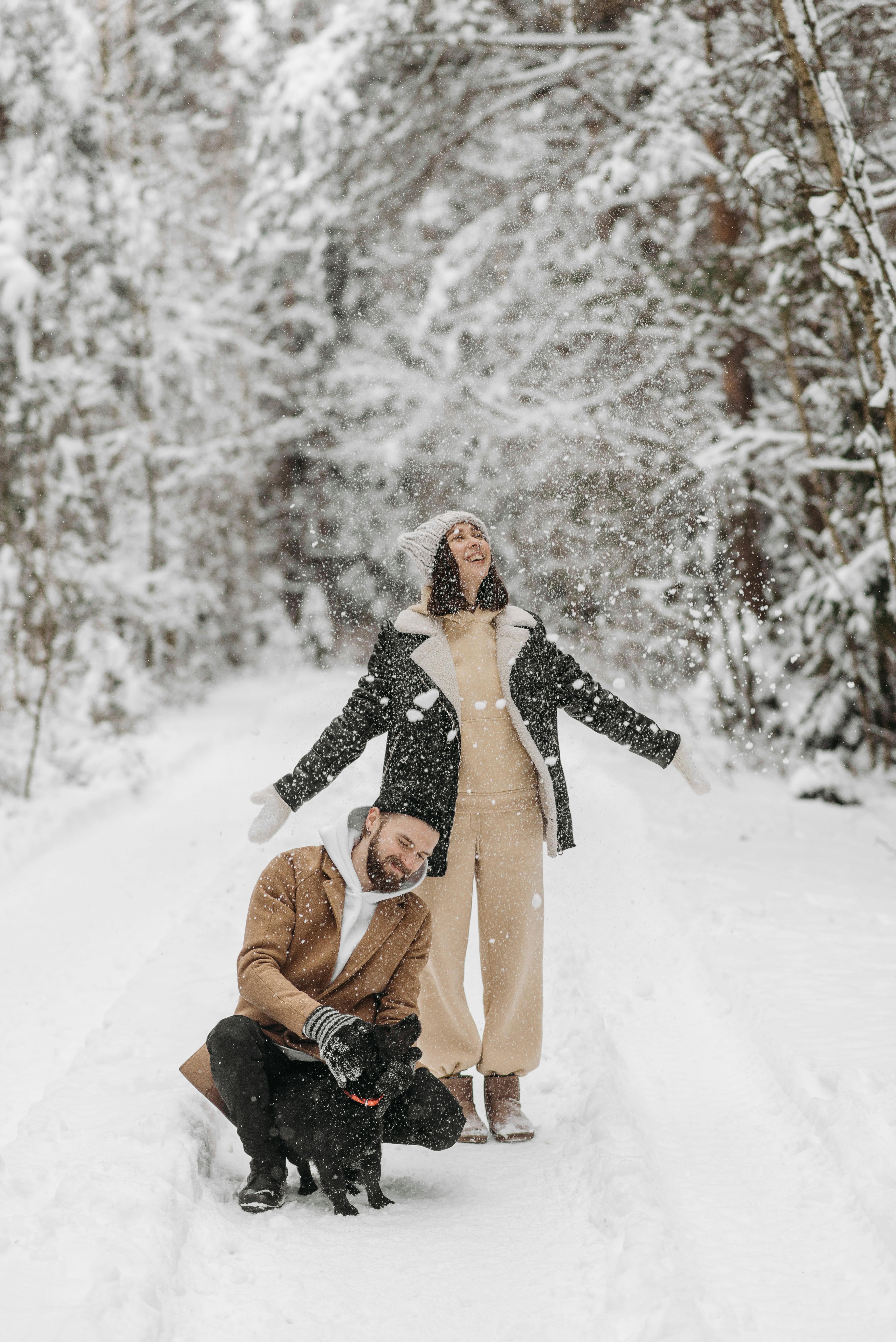 Happy couple enjoying a snowy winter day with their dog in a forest.