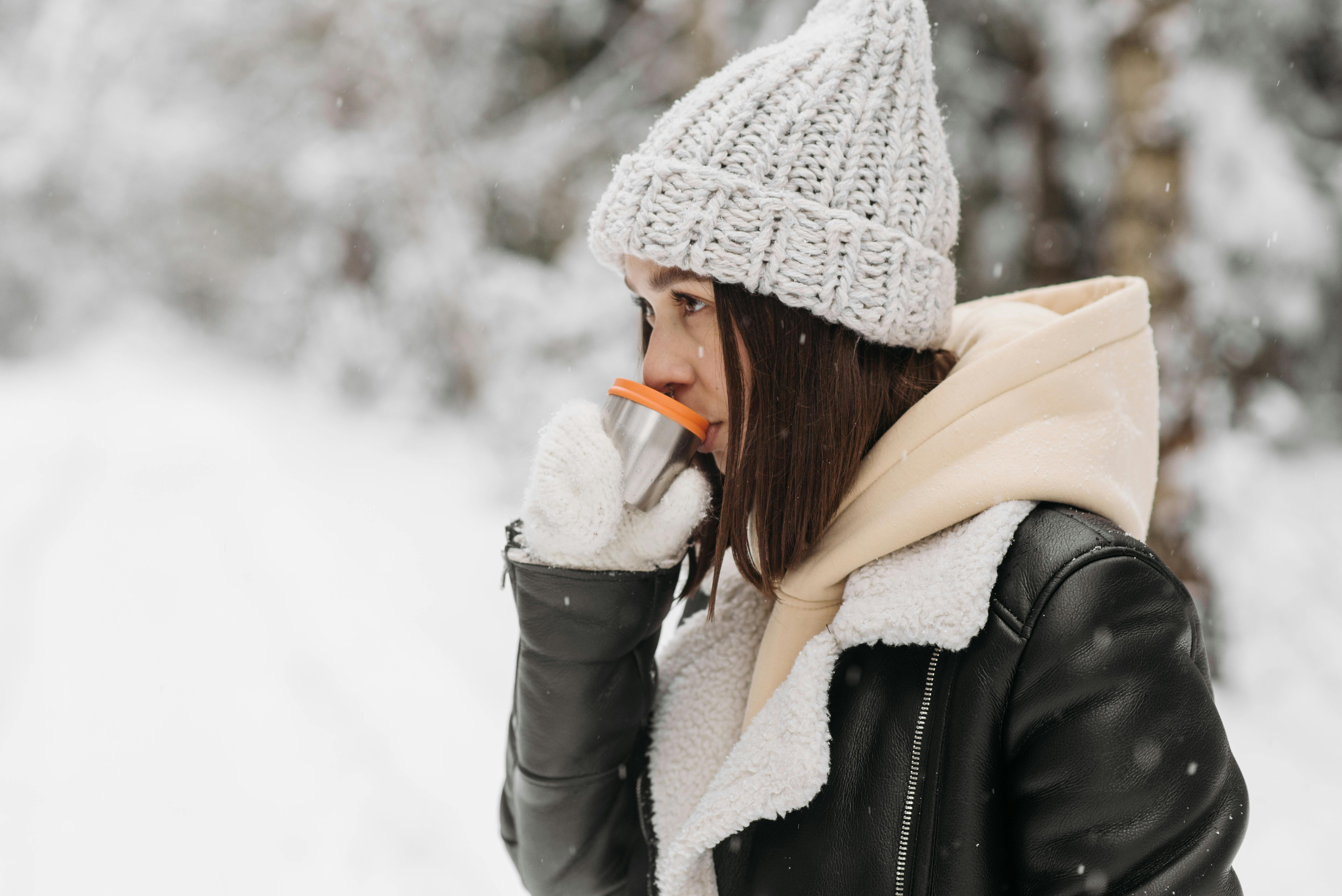 A woman in warm clothing enjoys a hot drink amidst a snowy winter landscape.