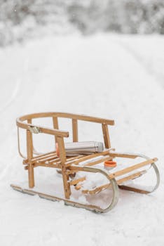 A wooden sledge with a vacuum flask sits on a snow-covered path in winter.
