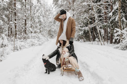 Couple with a dog and sled enjoying a snowy winter day in a forest setting.