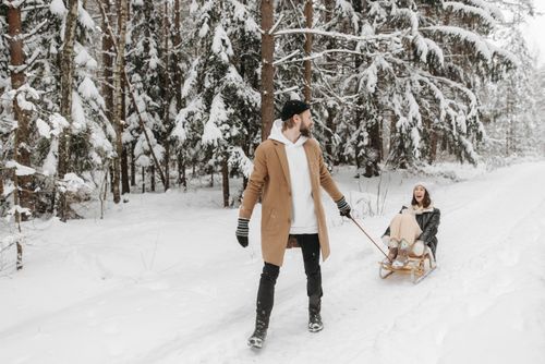Free A joyful couple having fun sledding in a snow-covered forest, capturing a playful winter moment. Stock Photo