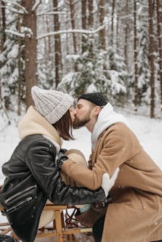 A couple shares a loving kiss amidst a serene snowy forest, creating a warm winter moment.