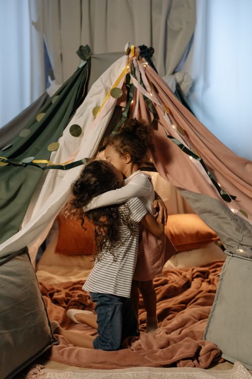 Free Two young girls share a hug inside a playful, cozy indoor tent decorated with blankets and pillows. Stock Photo