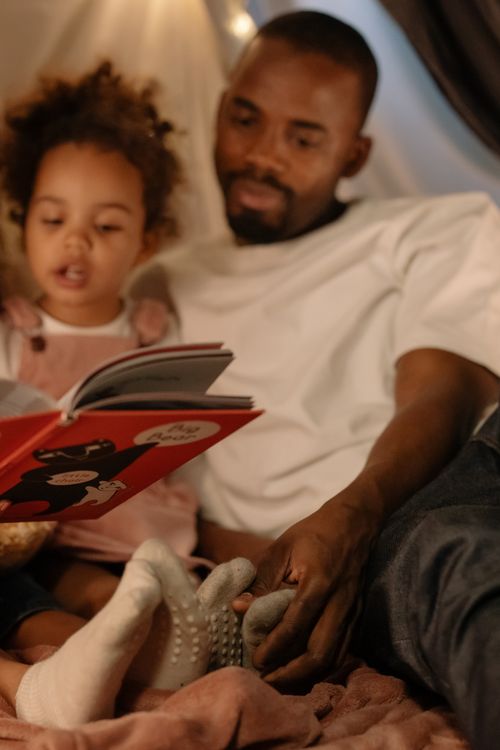 Free A loving father reads a storybook with his daughter, enjoying quality time indoors. Stock Photo