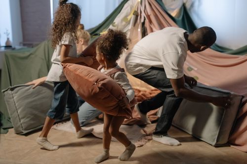 Free A playful family scene with a father and daughters having a pillow fight inside a cozy indoor fort. Stock Photo