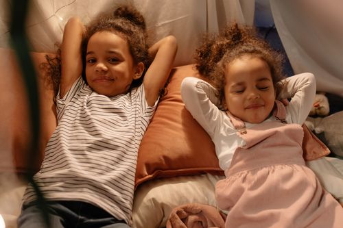 Free Two children lounging comfortably inside a cozy tent, surrounded by pillows, creating a warm and inviting atmosphere. Stock Photo