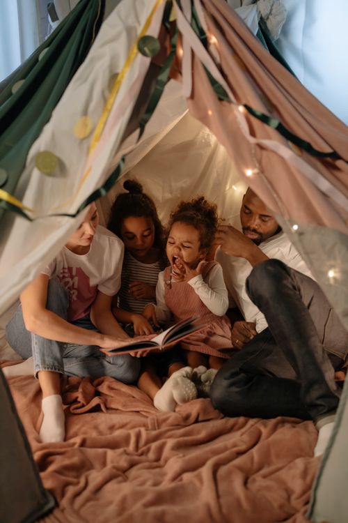 Free A diverse family reading together inside a cozy, indoor tent, creating a warm and joyful atmosphere. Stock Photo