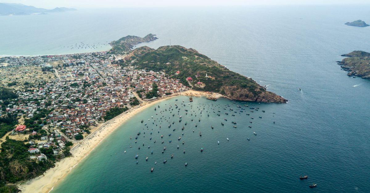 Explore the coastal beauty of Quy Nhon city with its busy harbor and lush green mountains from above.