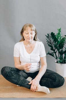 Elderly woman meditating indoors with incense, promoting relaxation and wellness.