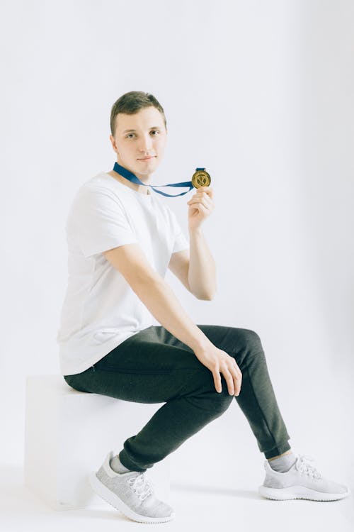 Man Sitting on White Stool Holding His Medal