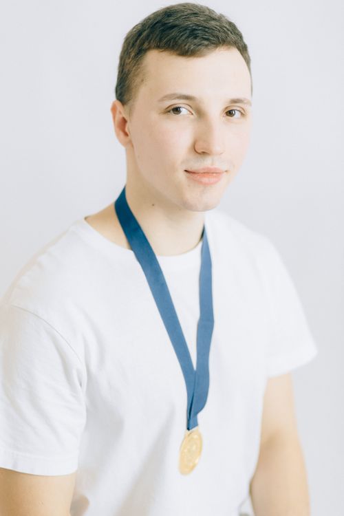Free Portrait of a young man wearing a gold medal and white shirt, symbolizing success. Stock Photo