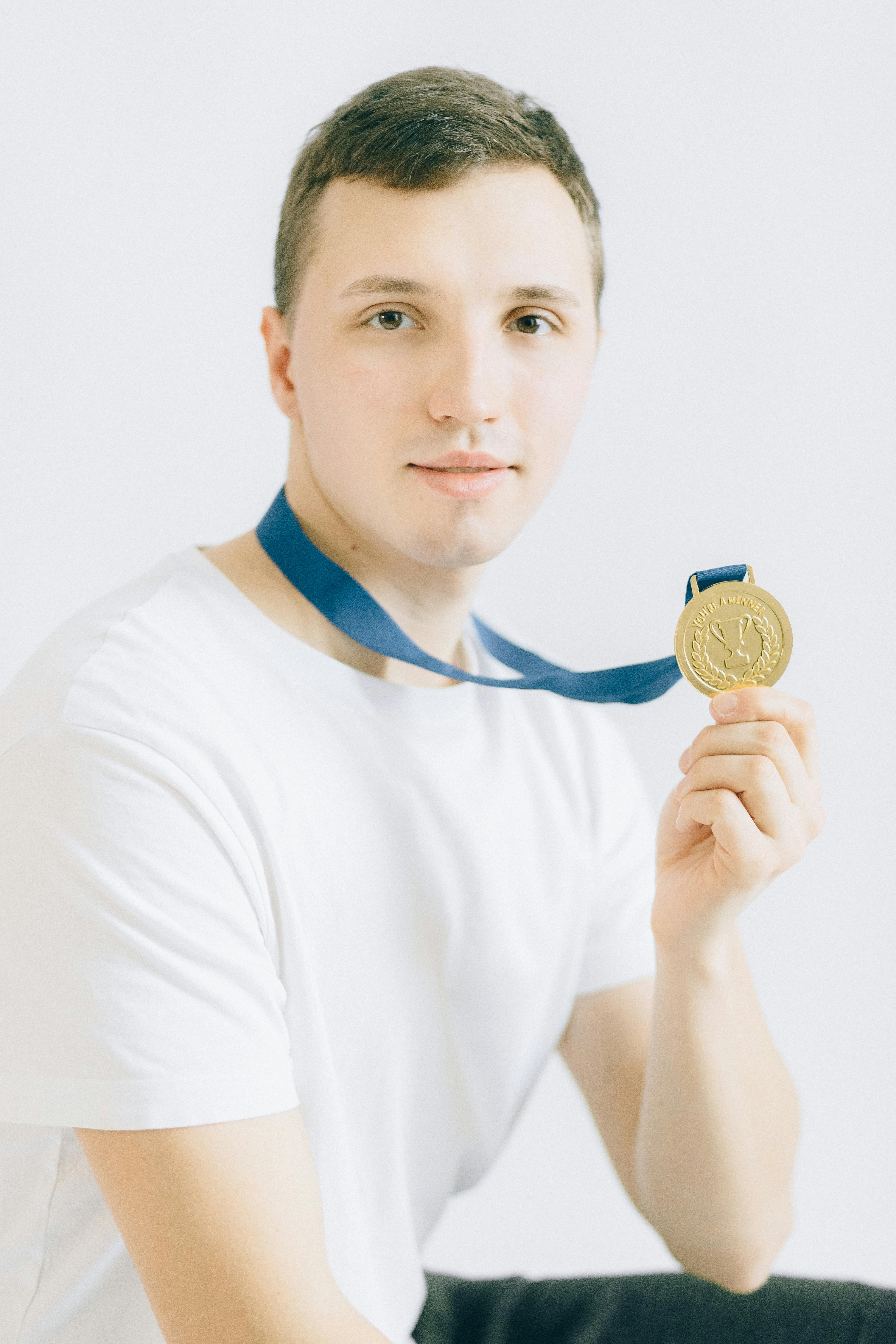 young man in white crew neck t shirt holding a gold medal