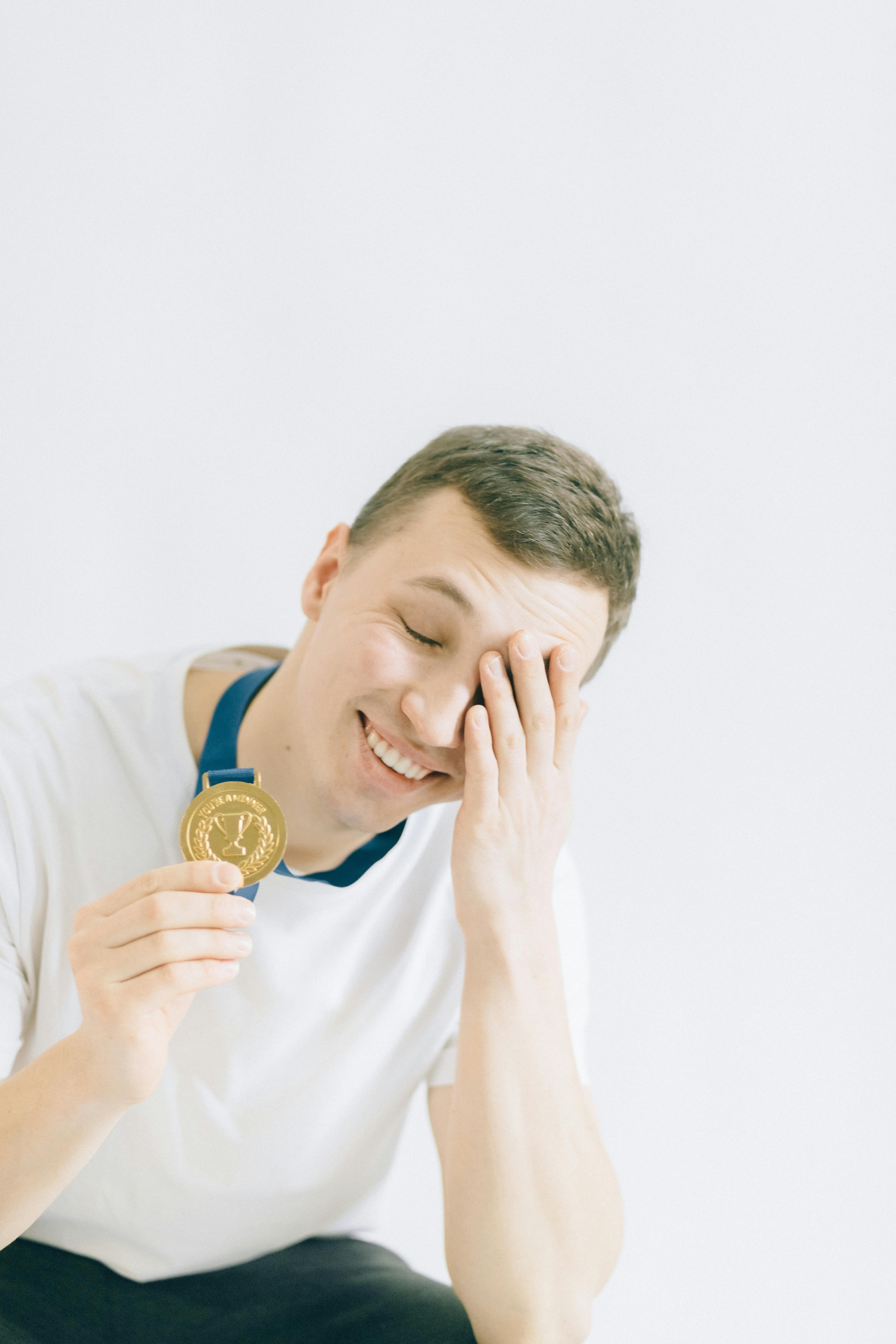 young man in white crew neck t shirt holding a gold medal