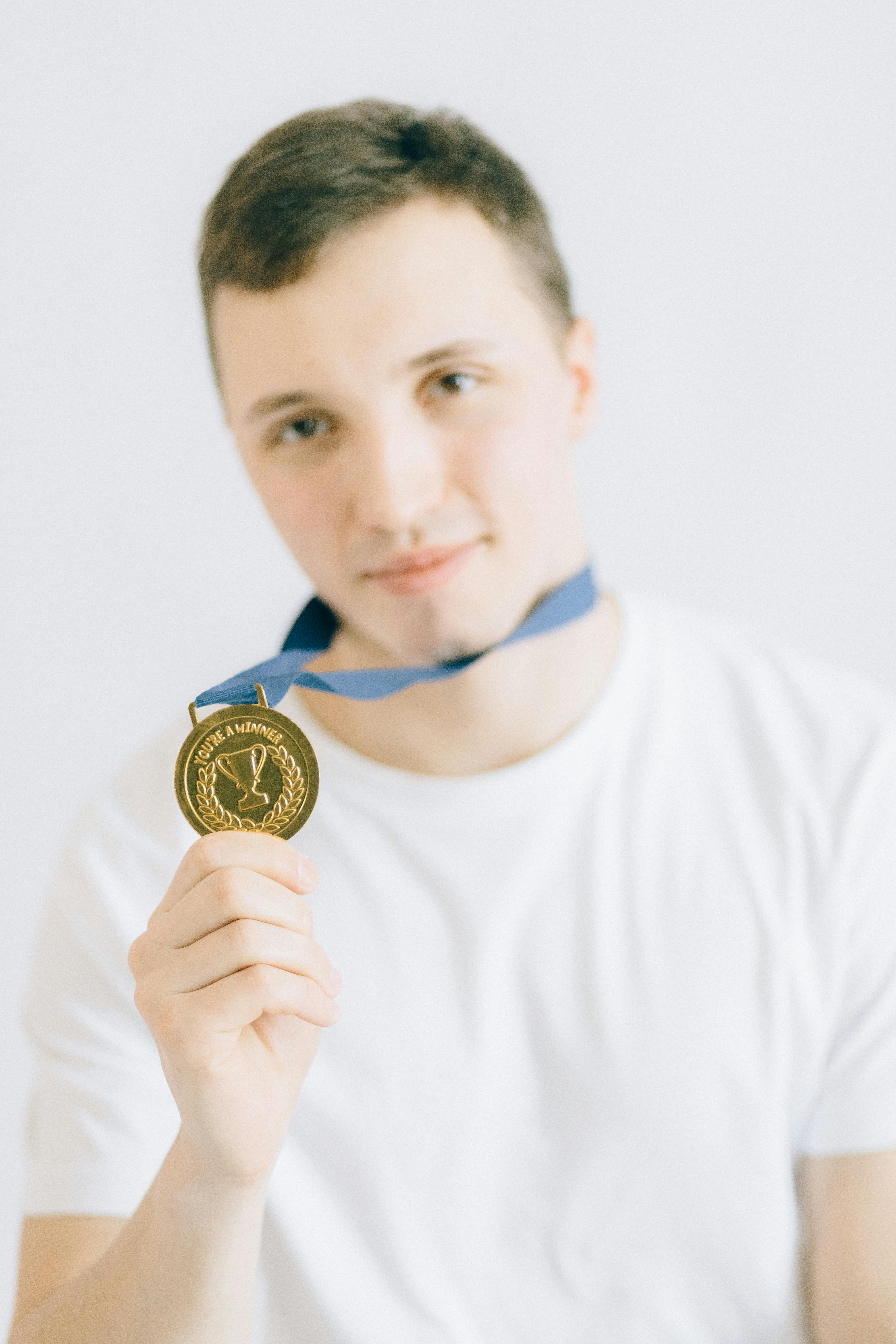 young man in white crew neck t shirt holding a gold medal