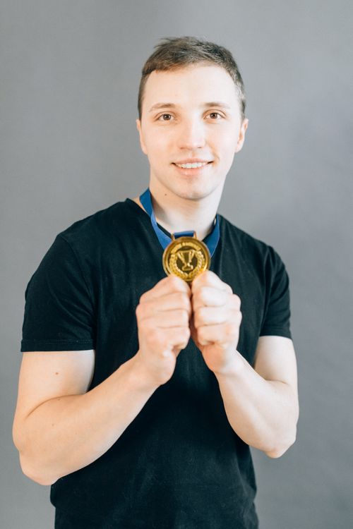 Free Smiling young man proudly holding a gold medal, symbolizing success and achievement. Stock Photo