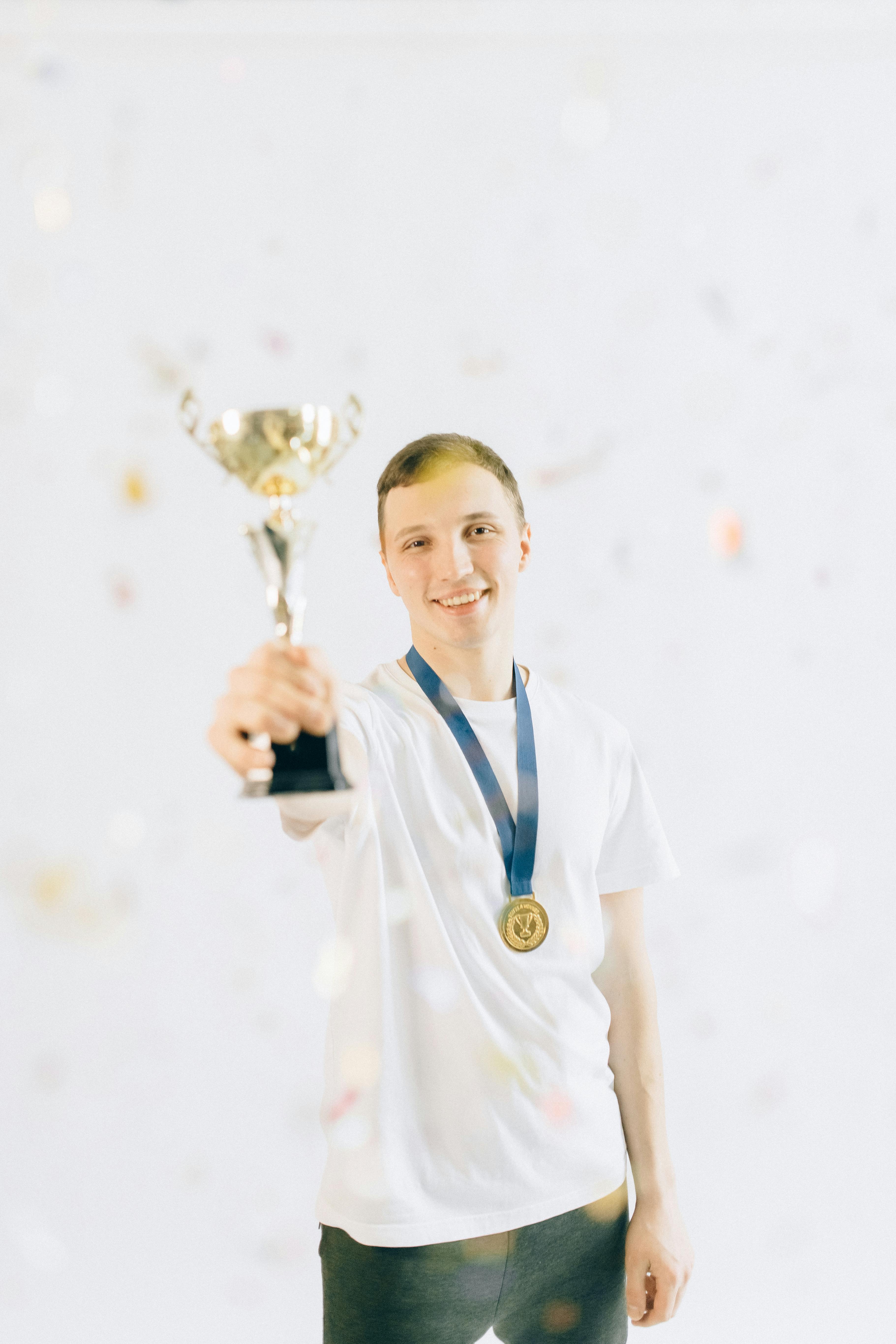 man in white crew neck shirt holding a trophy and wearing a gold medal