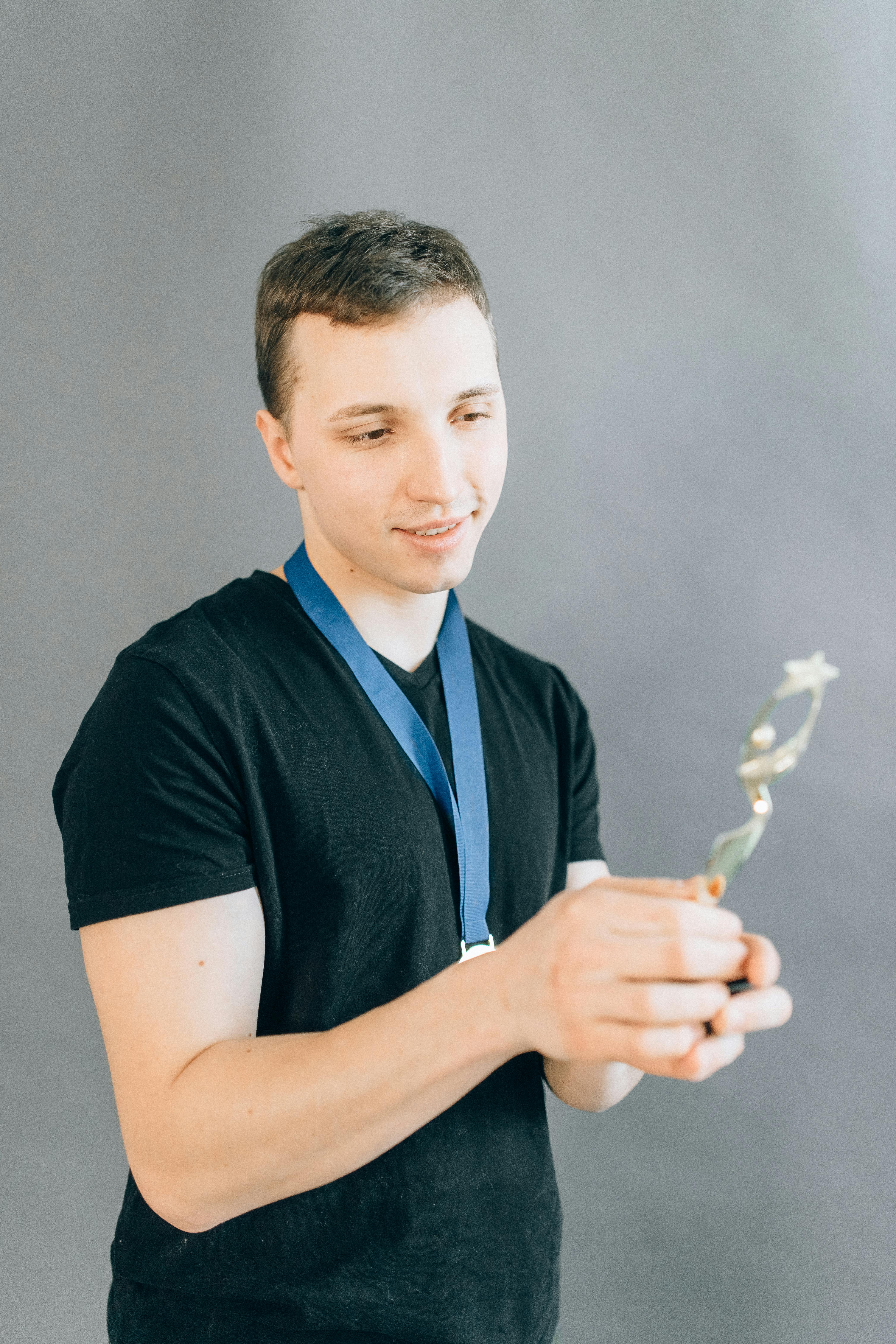 man in black crew neck shirt holding a trophy and wearing a gold medal