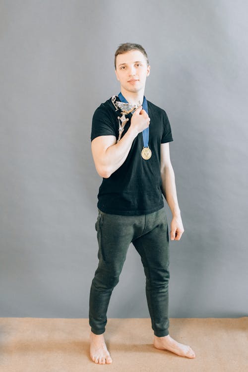 A Man in Black Shirt Holding a Trophy while Standing Near Gray Wall