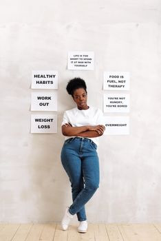 A woman standing against a wall with signs promoting healthy lifestyle habits and messages.
