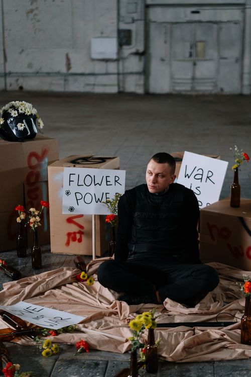 Free A protester sits among flowers and signs advocating nonviolence in an industrial setting. Stock Photo