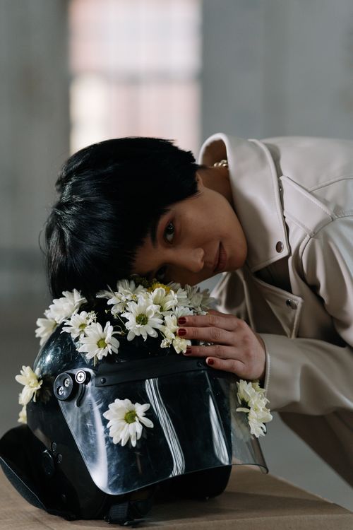Free Asian woman with short hair poses with a flower-adorned helmet, symbolizing peace and activism. Stock Photo