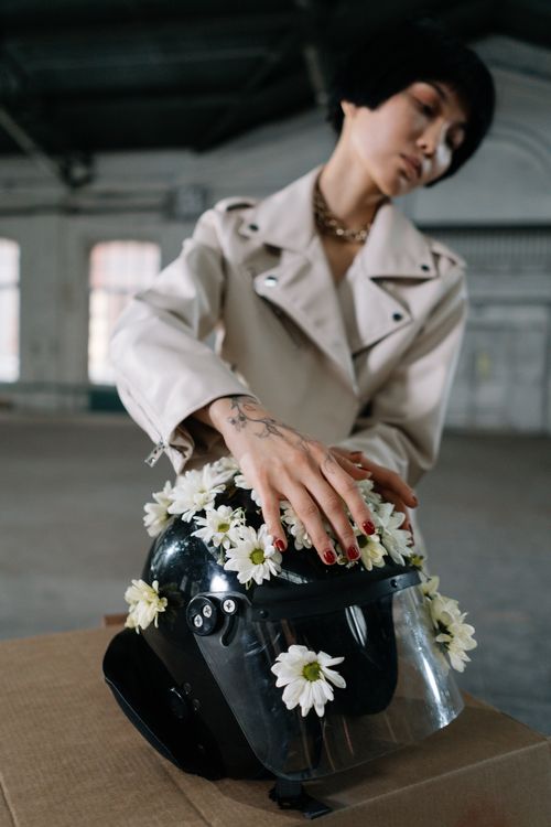 Free Asian woman in a beige jacket gently places flowers on a black helmet indoors. Stock Photo