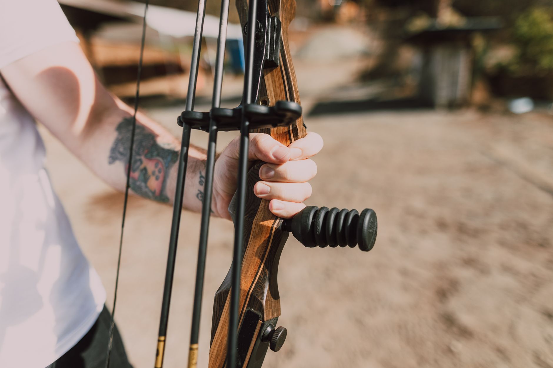 archery tag rental cairo — A close-up shot of a tattooed hand gripping a compound bow outdoors on a sunny day.