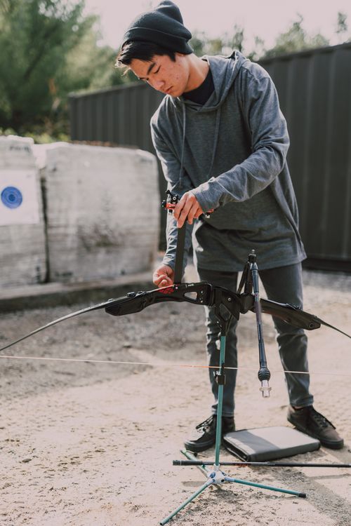 Free Young archer adjusting a compound bow at an outdoor archery range during the day. Stock Photo