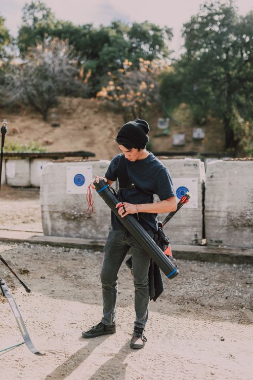 Free Young male archer prepares equipment at an outdoor archery range on a sunny day. Stock Photo