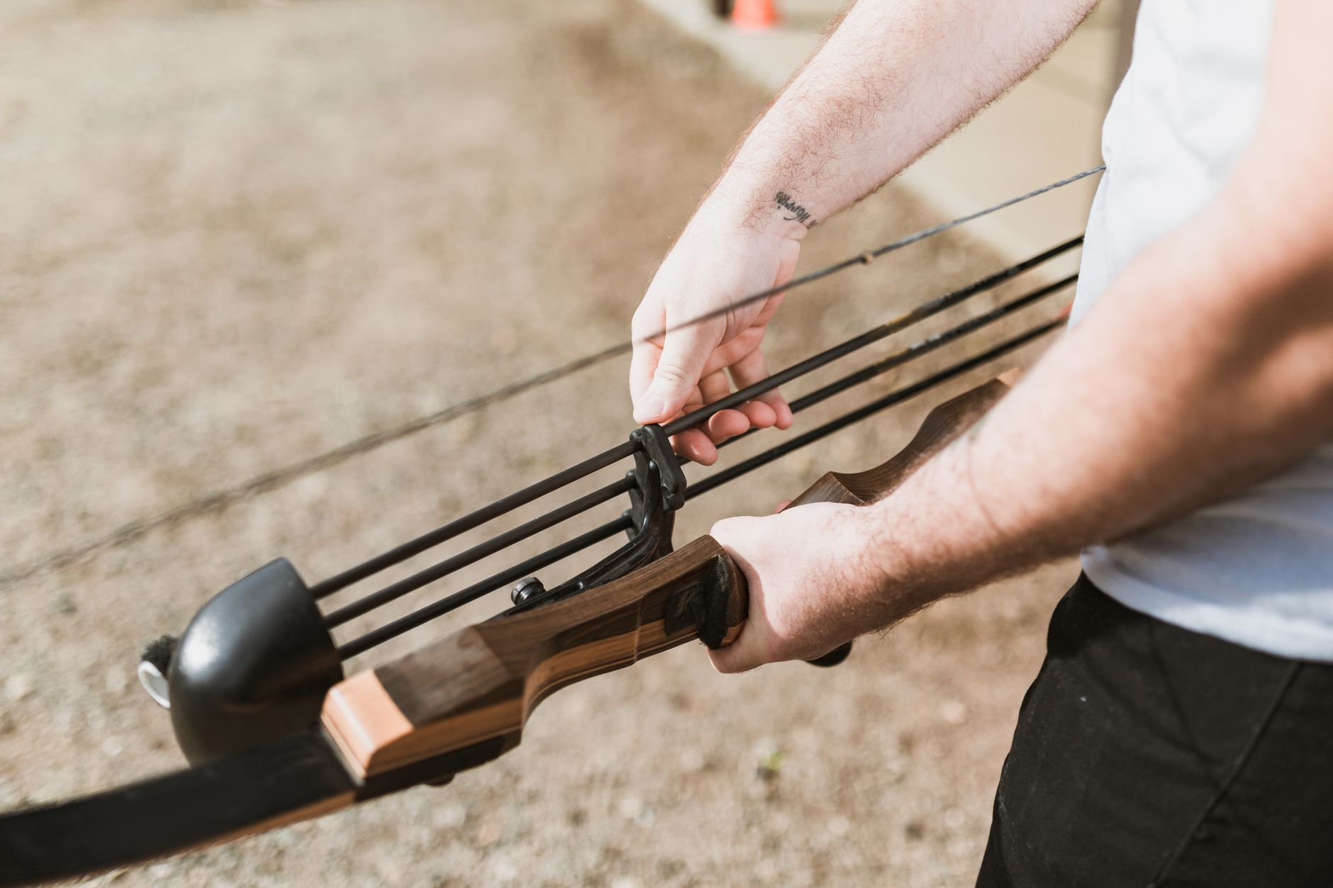 Close-up of a person preparing a recurve bow for archery practice outdoors.