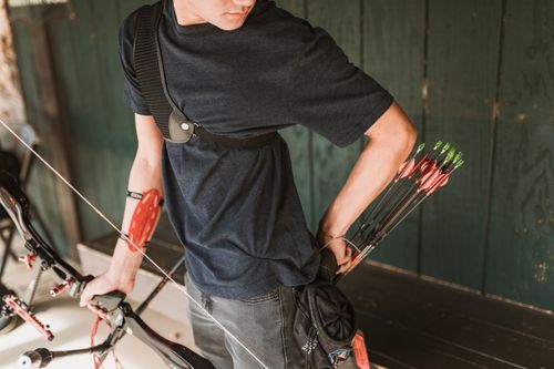 Free A young adult prepares his bow and arrows for archery practice indoors. Focused and ready. Stock Photo