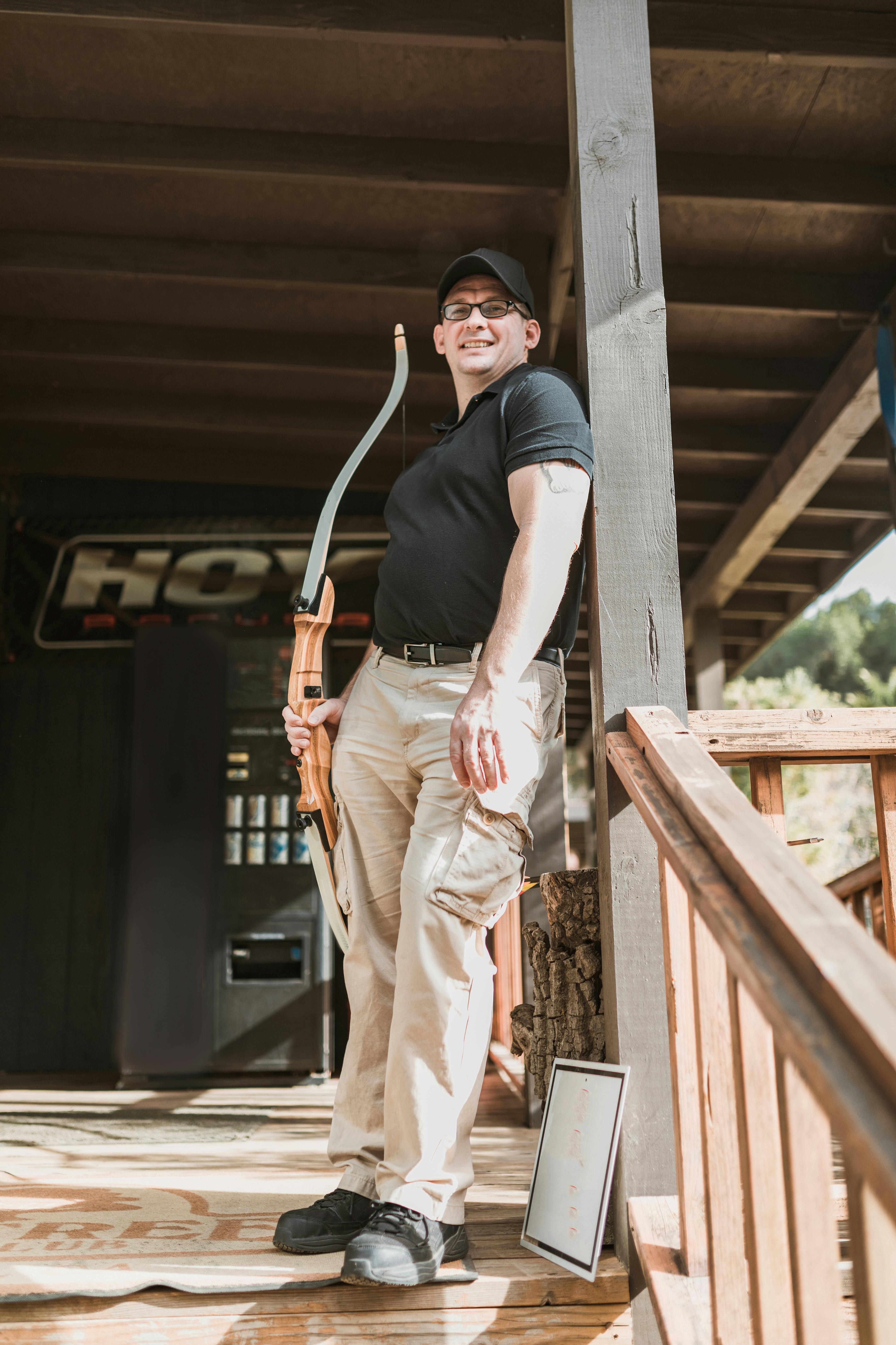 smiling young male archery coach with bow standing on wooden stairway