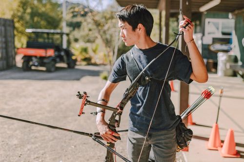 Free Young male archer practicing with a compound bow at an outdoor range on a sunny day. Stock Photo