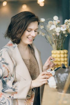Woman smiling while holding quail eggs next to floral vase in a cozy setting.