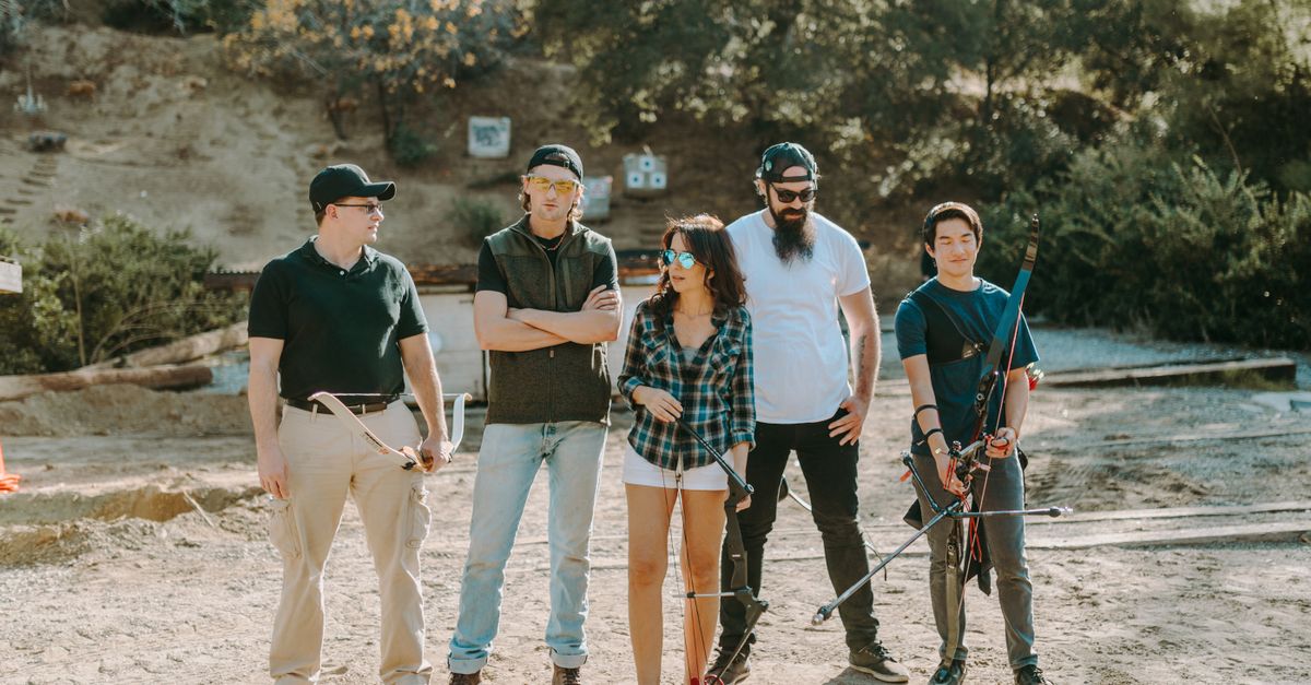 Five people practicing archery at an outdoor range under sunny conditions.
