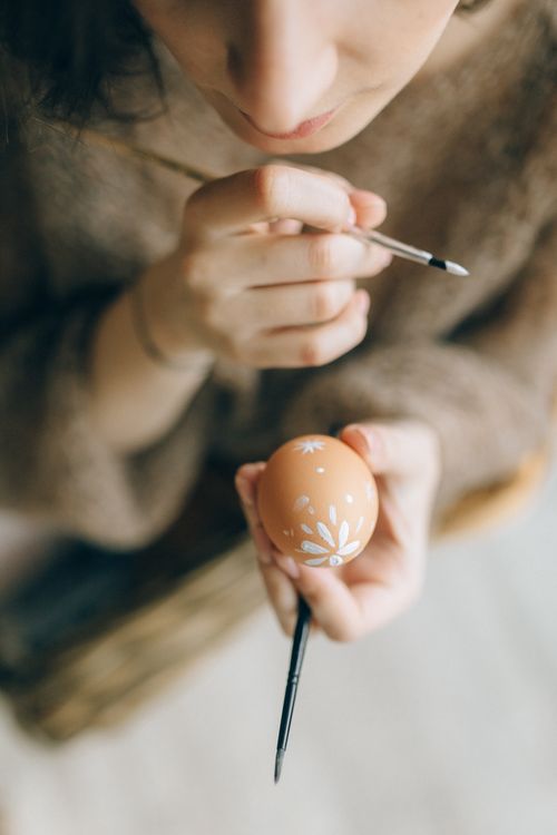 Free Close-up of a woman painting a decorative Easter egg with a brush indoors. Stock Photo