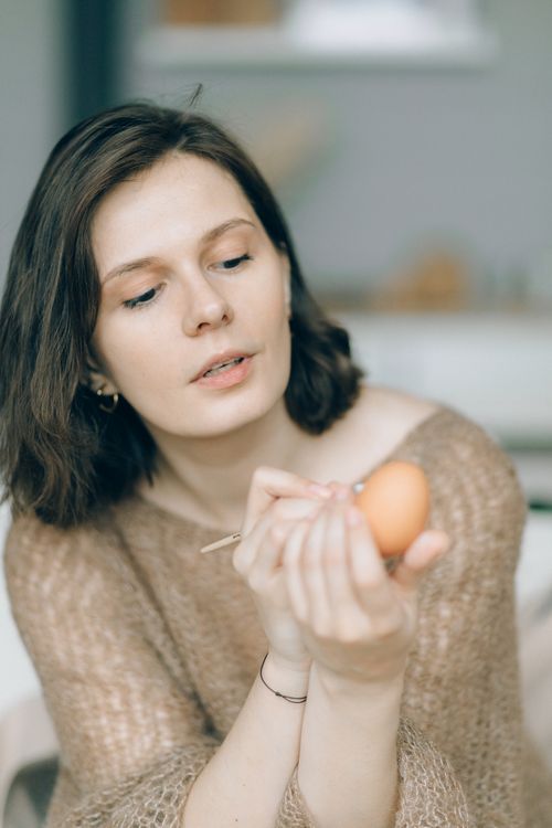 Free A woman carefully painting an Easter egg in a cozy indoor setting, embracing a festive and creative moment. Stock Photo