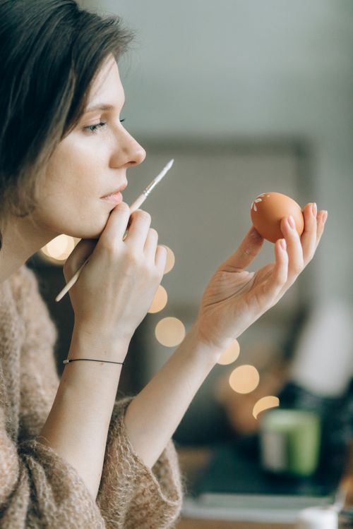Free Artistic side view of a woman painting an Easter egg with focus on creativity. Stock Photo