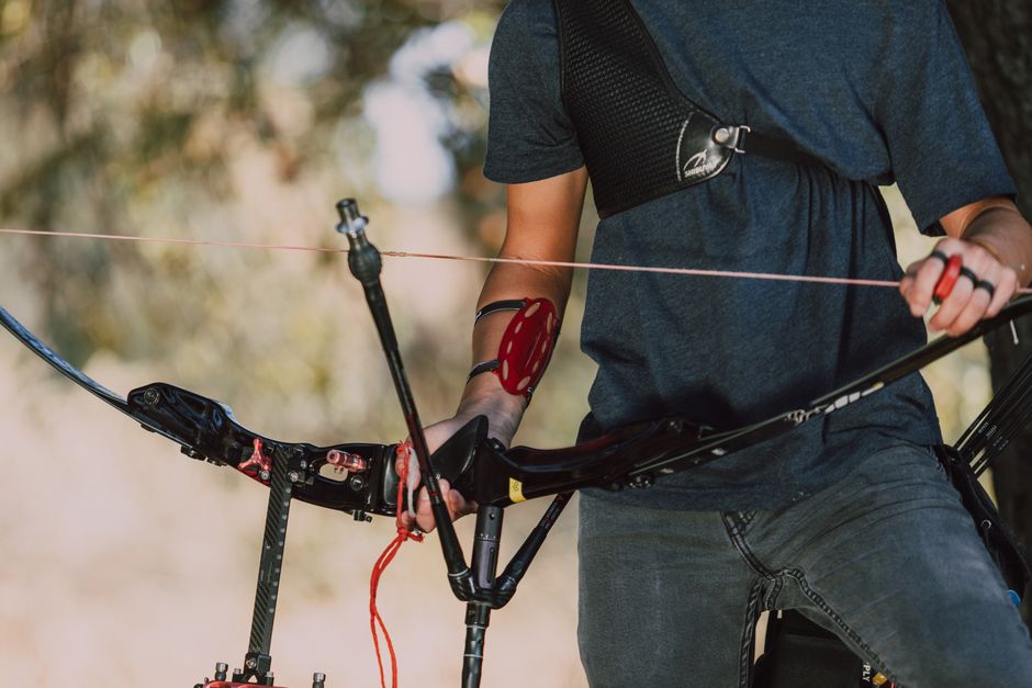A person equipped with archery gear outdoors, holding a recurve bow ready to shoot.