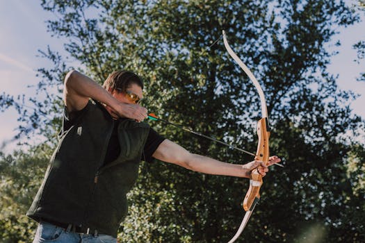 Man practicing archery with recurve bow outdoors on a sunny day.