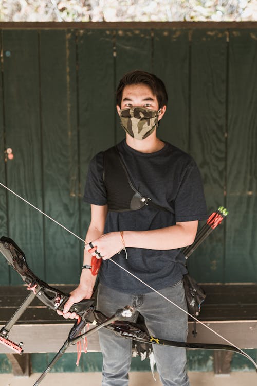 A Man in a Black Shirt and Denim Jeans Holding a Bow and Arrow