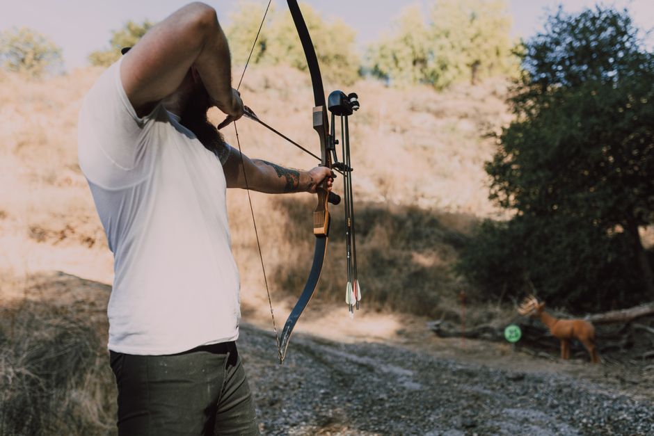 U.S. Army Veteran practicing traditional bow hunting in a wooded environment, focusing on form and precision