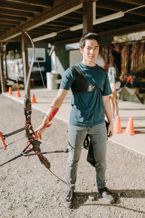 Free Young man in outdoor archery range holding a recurve bow, ready to shoot. Stock Photo