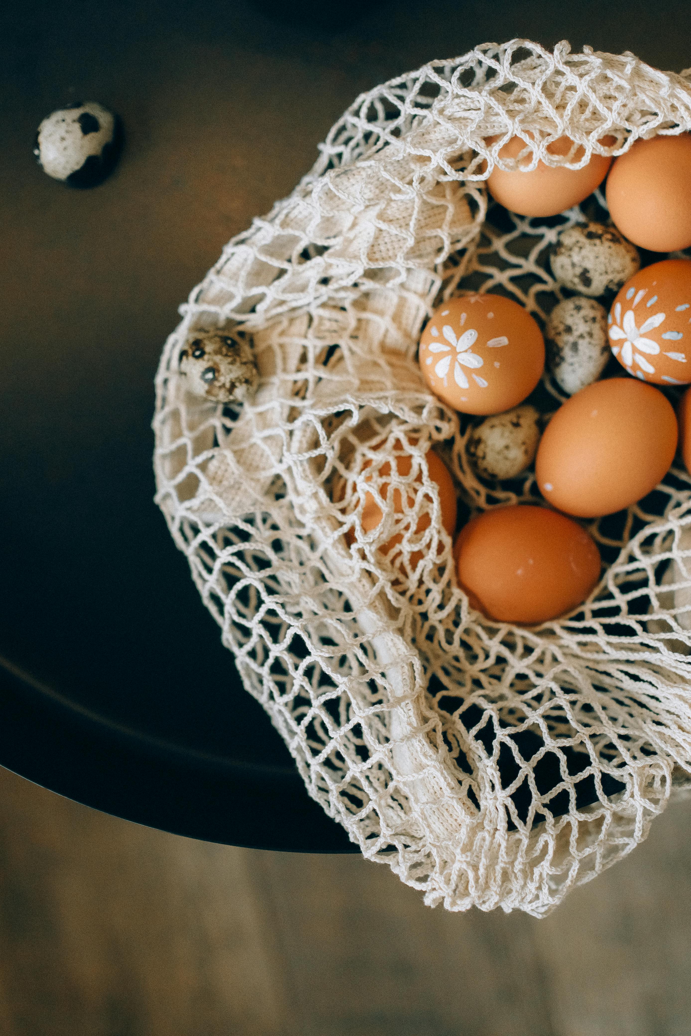 Decorated brown and quail eggs in a mesh bag on a dark surface. Top view.
