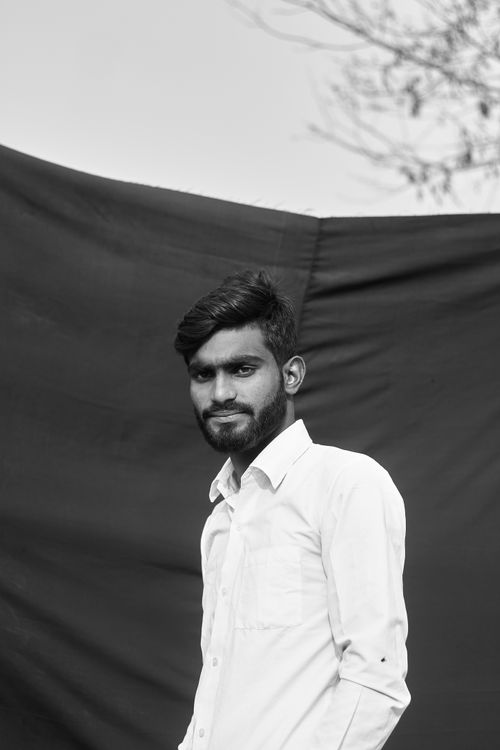 Free Monochrome portrait of a young man with facial hair, wearing a white shirt outdoors. Stock Photo